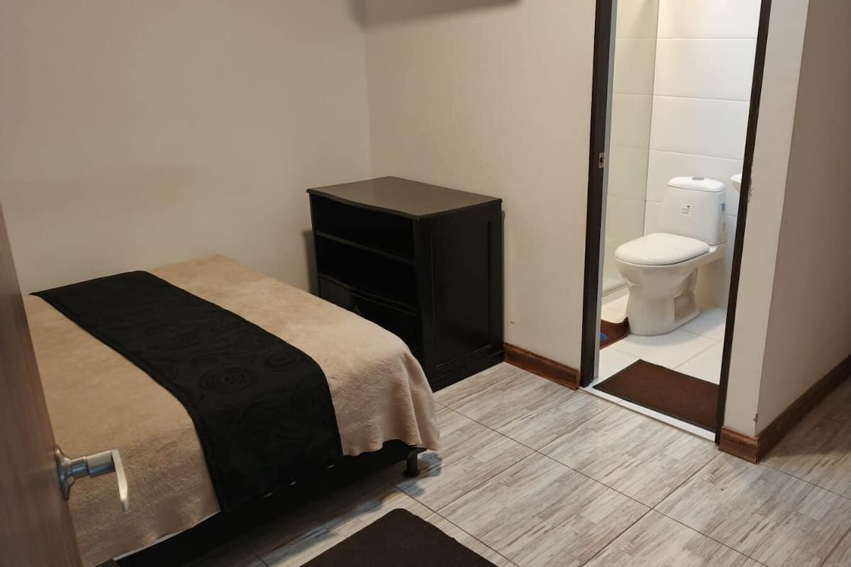 Ein kleiner, kompakter Raum mit einem Bett, einer schwarzen Ablage und einer weißen Toilette.