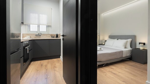 A modern hotel room with a bed, bedside tables, and a kitchen area with cabinets and appliances. - Luxury Glyfada flat steps from sea & main market (Glifada)