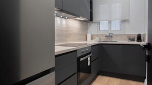 A modern kitchen with dark cabinetry, a stainless steel refrigerator, a wooden countertop, and a built-in oven. - Luxury Glyfada flat steps from sea & main market (Glifada)