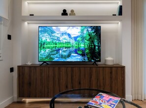 Ein Flachbildfernseher an einem Holzkabinett befestigt, mit einer Zeitschrift auf einem Glastisch davor.