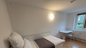 A small, modern room with a white sofa, a small table, and a window with a view of greenery.