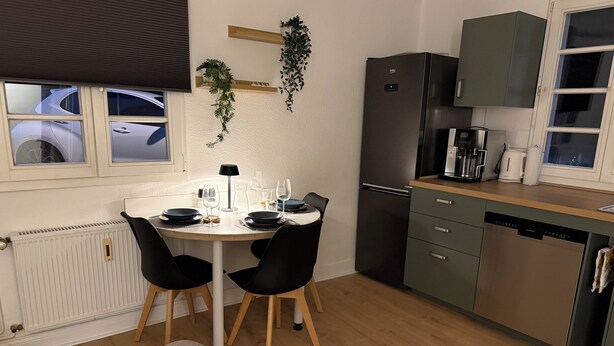 A modern kitchen with a dining table, chairs, a refrigerator, and a coffee maker.