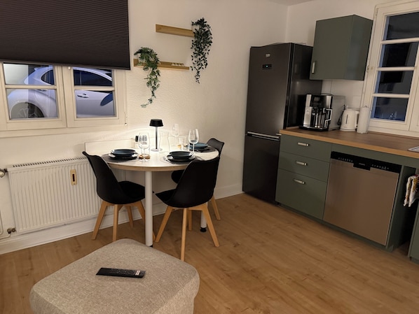 A modern kitchen with a dining table, chairs, a refrigerator, and a coffee maker.