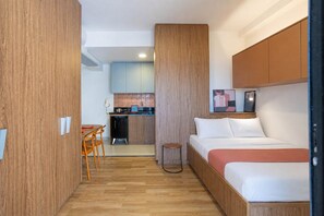 Une chambre d’hôtel compacte comprenant un lit, une petite kitchenette, un coin repas et un plancher en bois.