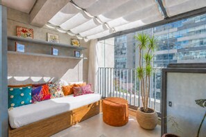 Un balcone con divano, cuscini, una pianta in vaso e vista sugli edifici.