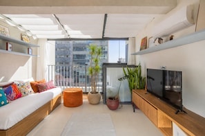 A modern living room with a sofa, ottoman, TV, and potted plants. - Harmonia da Vila (São Paulo)