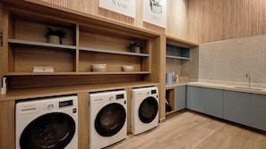 A laundry area with three washing machines, wooden shelves, and a sink. - Harmonia da Vila (São Paulo)
