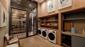 A laundry facility with three washing machines, wooden shelving, and a glass door entrance. - Harmonia da Vila (São Paulo)