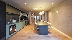 A modern kitchen with a central island, a dining area with a long table and chairs, and a hallway leading to another room. - Harmonia da Vila (São Paulo)