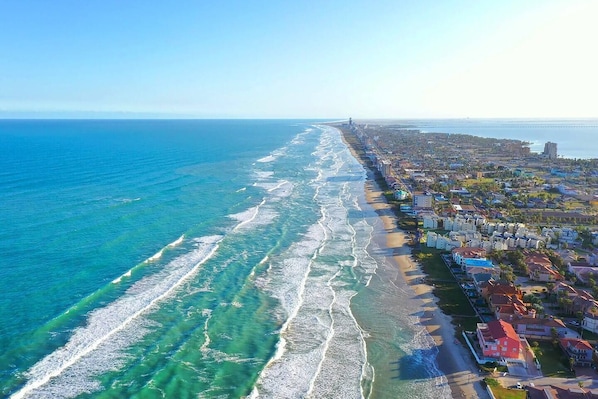 An aerial view of a coastal area with a beach, buildings, and a bridge.