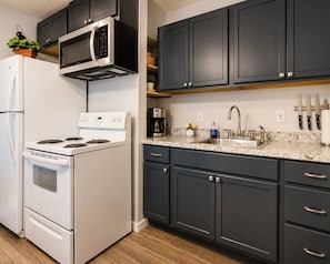 A kitchen with dark cabinets, a white refrigerator, a microwave, a stove, a sink, and a coffee maker.