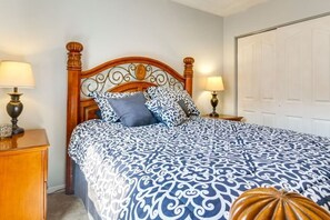 Un dormitorio con cabecera de madera, colcha estampada, dos lámparas de noche y una mesita de noche de madera.