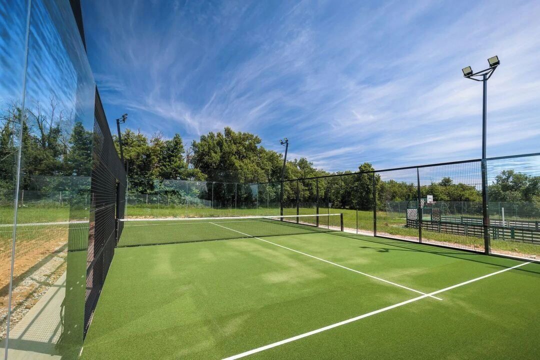 Ein Tennisplatz mit Netz, umzäunt und mit Bäumen im Hintergrund.