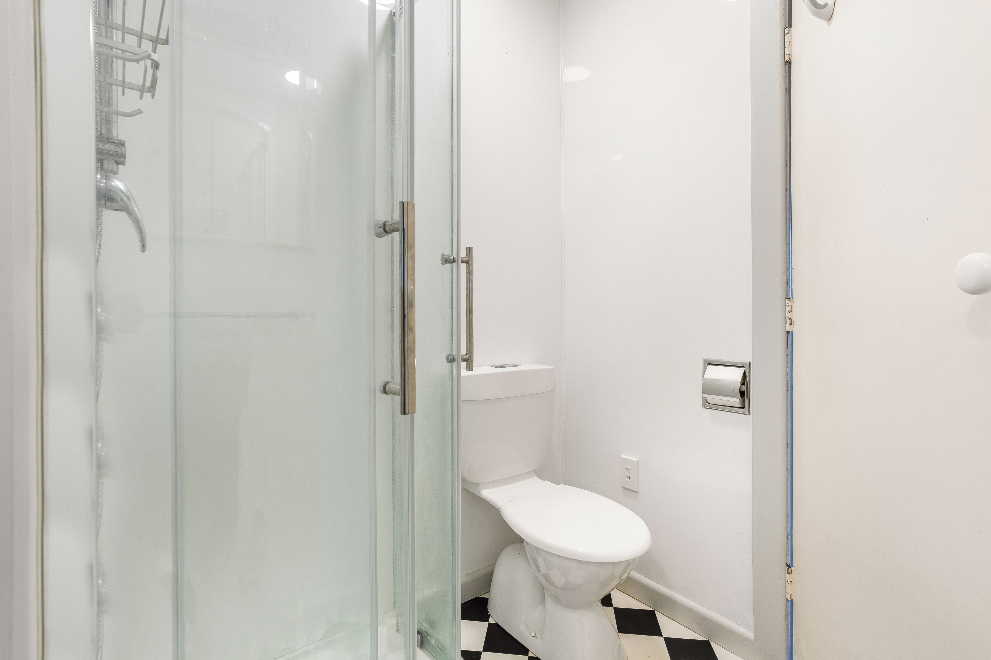 A bathroom with a glass shower enclosure, a white toilet, and a checkered floor.