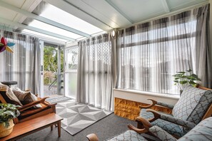 Une pièce baignée de lumière, avec un canapé, une chaise en bois, un tapis à motifs et une plante en pot.