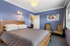 Ein Schlafzimmer mit einem großen Bett, einem hölzernen Kopfteil, einem Stuhl, einem Spiegel und einem Buntglasfenster.