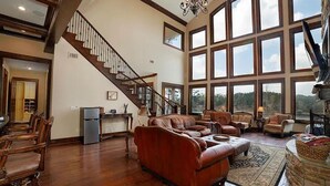 Ein geräumiges Wohnzimmer mit einem großen braunen Ledersofa, einem Essbereich mit Holzsesseln, einer Küchenzeile und einer Treppe, die in einen oberen Bereich führt.