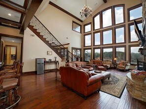 A spacious living room with a large brown leather sofa, a dining area with wooden chairs, a kitchen area, and a staircase leading to an upper level. - Spectacular 4-bedroom house on beautiful Lake Wedowee (Wedowee)