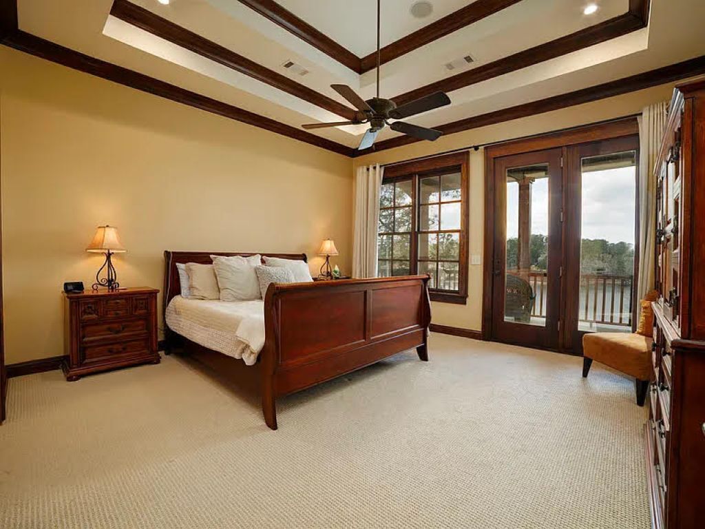 A bedroom with a bed, a nightstand, a lamp, a ceiling fan, and large windows.