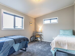 A bedroom with two beds, a shelf with items, and two windows. - Mountainview Glimpse - Ohakune Holiday Home (Ohakune)
