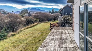 Une terrasse en bois mène à un bâtiment moderne doté de grandes fenêtres, avec une pelouse et des montagnes en arrière-plan.