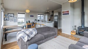 Un espace de vie moderne comprenant un canapé gris, une table à manger en bois, un coin cuisine et un poêle à bois.