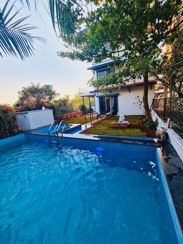 A swimming pool with a clear blue water, a patio area with outdoor furniture, and a building with a white facade and blue trim.