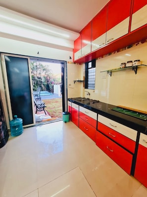 A kitchen with red cabinets, a black countertop, and a sliding glass door leading to an outdoor area.