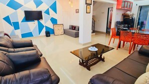 Un salon moderne doté d’un téléviseur à écran plat, d’un ventilateur de plafond et d’un coin repas avec des chaises rouges.