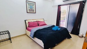 Une chambre à coucher comprenant un lit, un ventilateur de plafond, un appareil de climatisation, une fenêtre avec des rideaux et un tableau encadré accroché au mur.