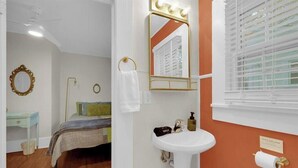 Ein Schlafzimmer mit einem Bett, einem Schminktisch mit Spiegel, einem Waschbecken und einem Fenster mit Jalousien.
