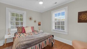 Ein Schlafzimmer mit einem Bett, zwei Nachttischen, einem Fenster und einem Deckenventilator.