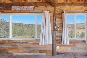 Eine rustikale Holzhütte mit Holzwänden, einem Schild mit der Aufschrift 'American Cowboy' und zwei Fenstern mit Vorhängen.