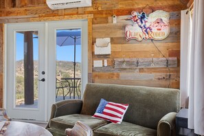 Ein Zimmer mit Holzwand, einer Couch mit Kopfkissen in den Farben der US-amerikanischen Flagge, einer Tür zu einer Außenpatio und einem Wandzeichen mit Rodeo-Dekorationen.