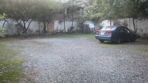 Un camí de grava que condueix a un cotxe estacionat en una zona residencial amb arbres i una paret blanca.