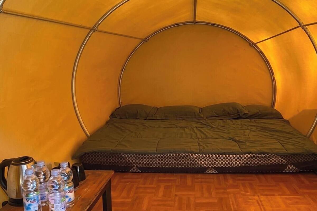 A tent with a bed, a table with water bottles, and a kettle.