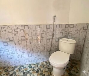 A bathroom with a toilet, a shower, and a patterned wall. - Cozzy Saung Singkur Riverside (bandung)