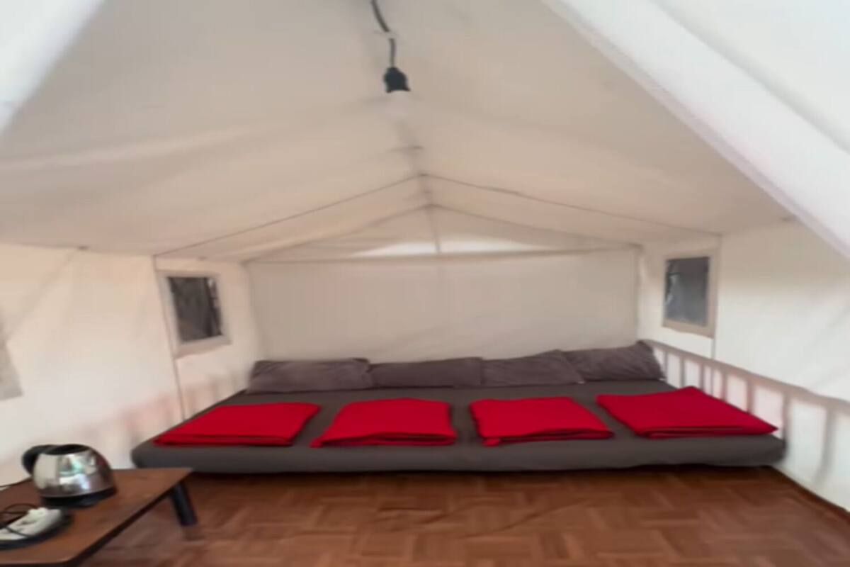 A tented room with a bed, pillows, a table with a kettle, and a window.