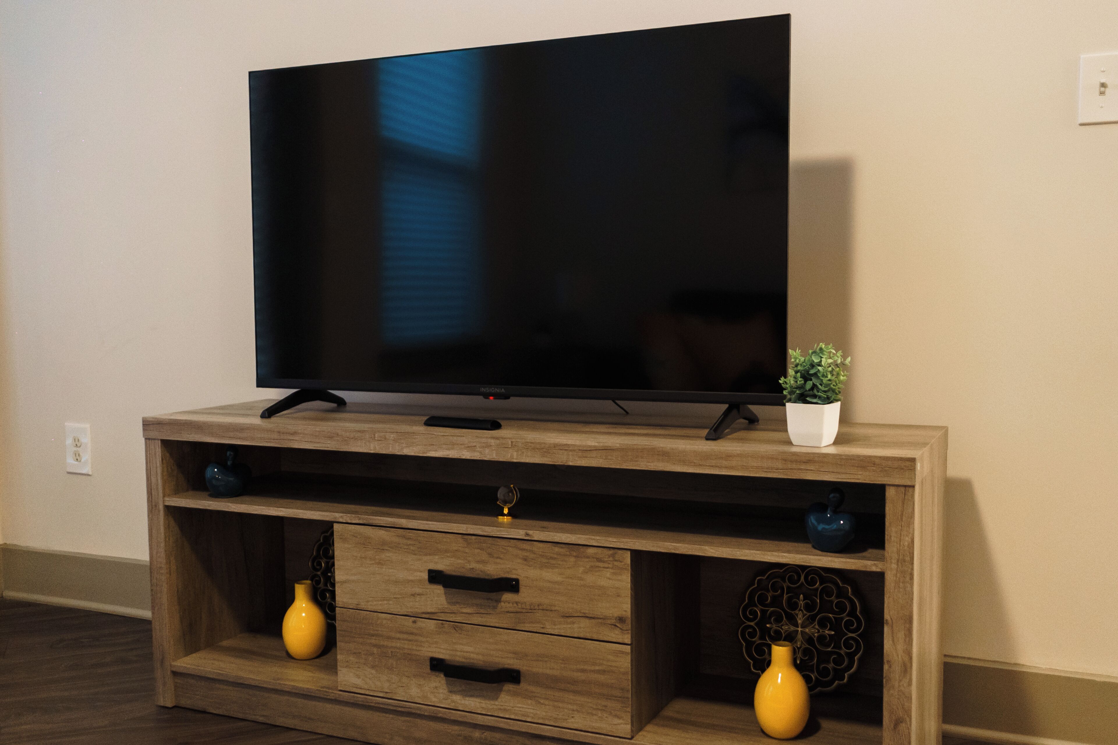 A flat-screen TV on a wooden entertainment center with two drawers and two vases.