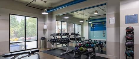 A gym with weightlifting equipment, a bench, kettlebells, and a mirror.