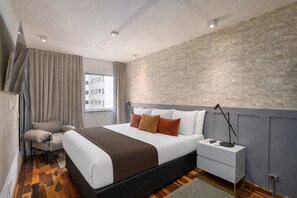 Ein modernes Hotelzimmer mit Bett, Nachttisch, Lampe und Blick auf die Stadt durch das Fenster.