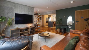 Una sala de estar moderna con televisor de pantalla plana, sofás de cuero, una mesa de centro y una cocina al fondo.