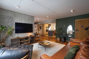 Ein modernes Wohnzimmer mit Flachbildfernseher, Ledersofas, einem Couchtisch und einer Küche im Hintergrund.