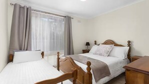 Hotellihuone, jossa on kaksi sänkyä, puinen pääty, yöpöytä lampulla ja ikkuna, jossa on verhot.