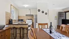 A kitchen with a microwave, stove, refrigerator, and bar stools. - The Moorings Tides & Tails - Pets Welcome! (St Leonards)