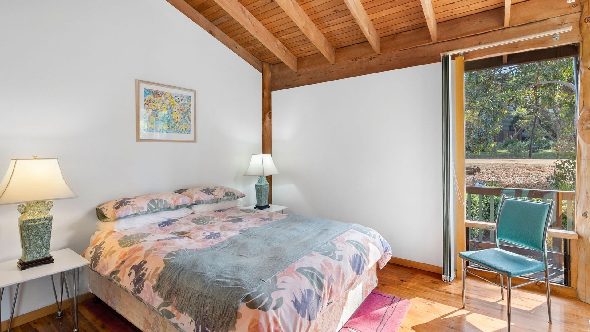 A bedroom with a bed, two bedside lamps, a window with a view, and a chair.