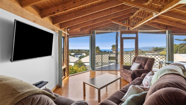 Ein großzügiger Wohnbereich mit Holzboden, einem Flachbildfernseher, einer Couch und Blick aufs Meer.