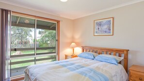 Ein Schlafzimmer mit Bett, Nachttisch, Lampe, einem Fenster mit Vorhängen und einem Gemälde an der Wand.