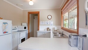 A compact kitchen with a refrigerator, microwave, oven, sink, and a window with a view. - The Sundowner Cottage - Central Torquay (Torquay)