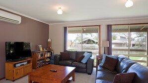 A living room with a television, sofa, coffee table, and a bookshelf. - The Sundowner Cottage - Central Torquay (Torquay)